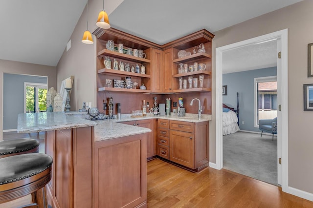 bar featuring hanging light fixtures, a sink, light wood-style floors, baseboards, and wet bar