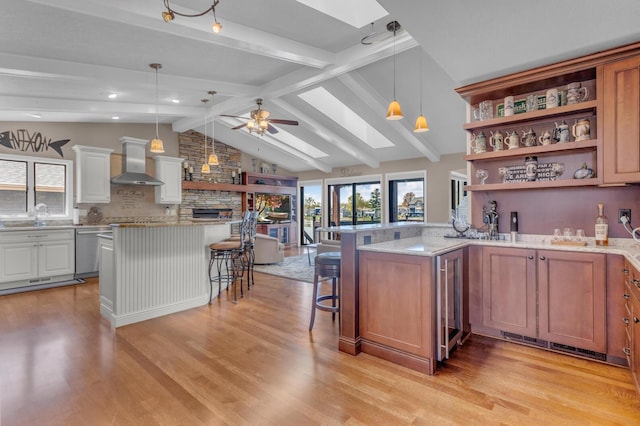 kitchen featuring stainless steel dishwasher, lofted ceiling with skylight, a breakfast bar area, wall chimney range hood, and a sink