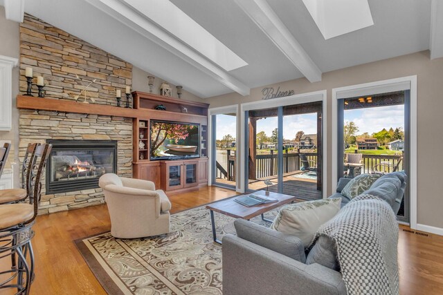 living room with visible vents, wood finished floors, vaulted ceiling with skylight, and a fireplace