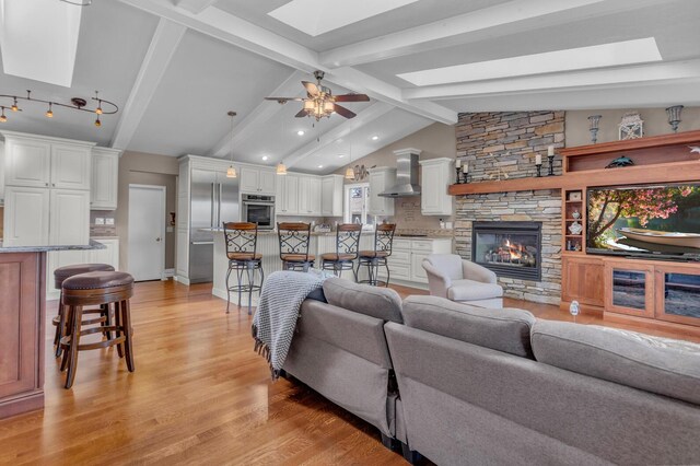 living room featuring a ceiling fan, light wood-type flooring, a stone fireplace, and lofted ceiling with skylight