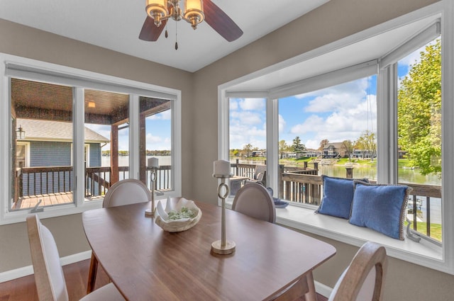 dining area with a water view, ceiling fan, and baseboards