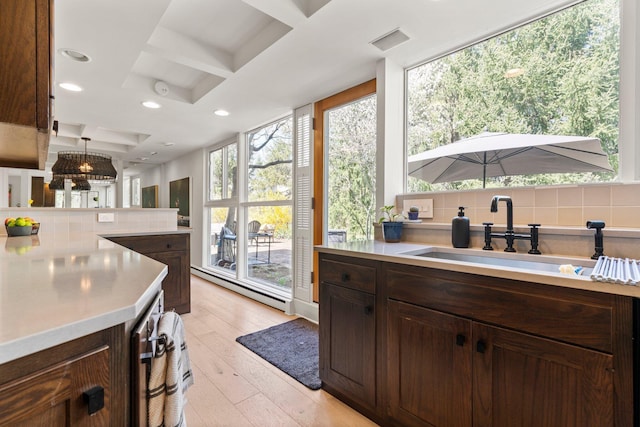 kitchen with dark brown cabinets, a sink, light countertops, decorative backsplash, and coffered ceiling