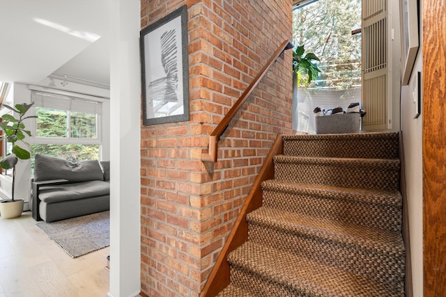 stairs featuring brick wall and wood finished floors