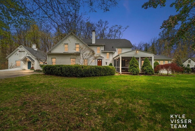 traditional home with a chimney, a sunroom, and a front lawn