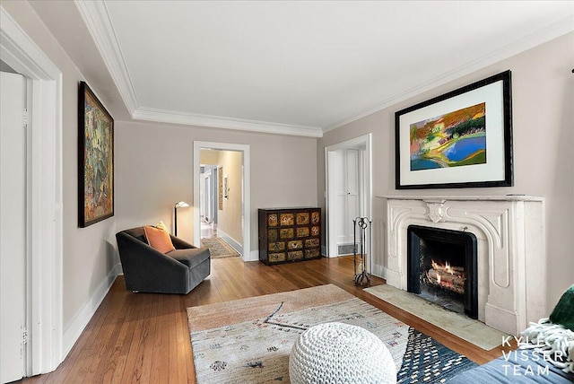 living room featuring a fireplace, wood-type flooring, baseboards, visible vents, and ornamental molding