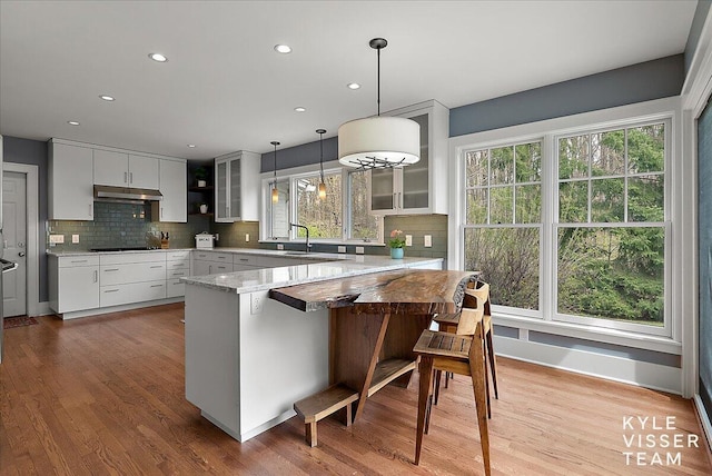 kitchen with under cabinet range hood, black electric stovetop, glass insert cabinets, and a wealth of natural light