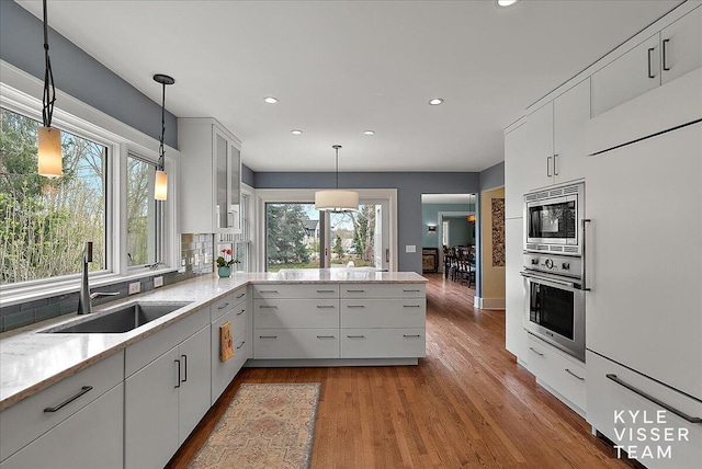 kitchen featuring wood finished floors, a sink, a peninsula, built in appliances, and recessed lighting