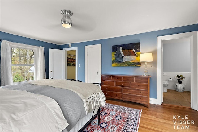 bedroom with ensuite bathroom, baseboards, and wood finished floors
