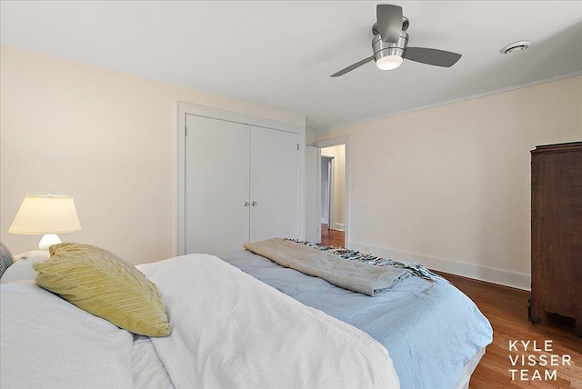 bedroom with ceiling fan, wood finished floors, baseboards, a closet, and ornamental molding