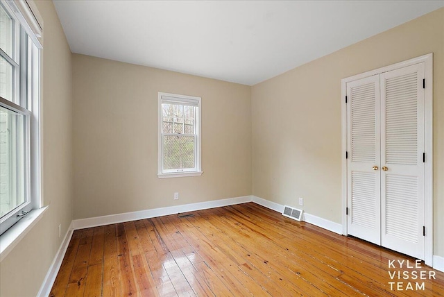 unfurnished bedroom featuring light wood-style floors, baseboards, a closet, and visible vents