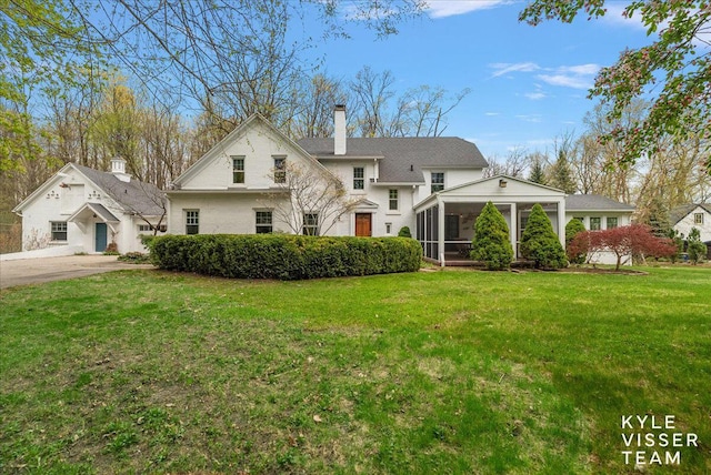 view of front of home featuring a sunroom, a front yard, and a chimney