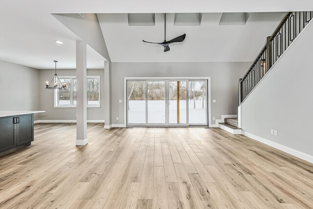 5182 Grande View Ln, Jackson, MI 49201 - unfurnished living room featuring light wood finished floors, ceiling fan with notable chandelier, baseboards, vaulted ceiling, and stairway