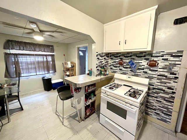 kitchen with ceiling fan, tile countertops, white range with gas cooktop, white cabinets, and backsplash