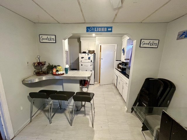 kitchen featuring arched walkways, white cabinets, freestanding refrigerator, a peninsula, and a breakfast bar