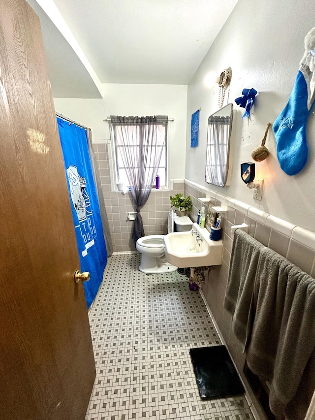bathroom with wainscoting, toilet, tile patterned floors, a shower with shower curtain, and tile walls
