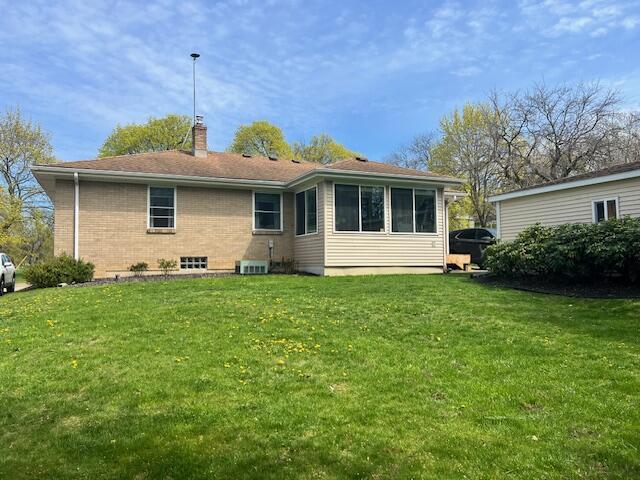back of house featuring a lawn, brick siding, and a chimney