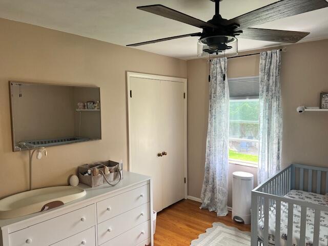 bedroom featuring a nursery area, a ceiling fan, and light wood-type flooring
