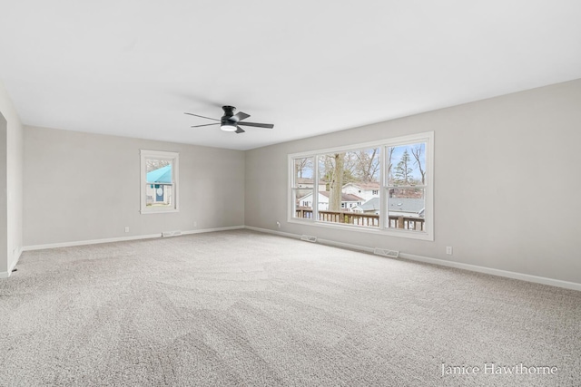 carpeted empty room with visible vents, ceiling fan, plenty of natural light, and baseboards