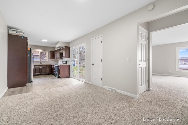 unfurnished living room featuring a sink, visible vents, light colored carpet, and baseboards