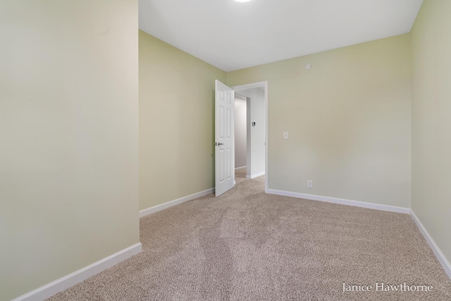 spare room featuring light colored carpet and baseboards