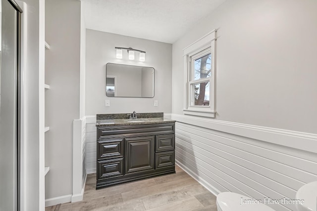bathroom with wood finished floors, toilet, vanity, and baseboards