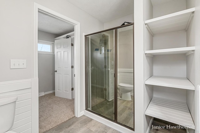 bathroom featuring baseboards, wood finished floors, a shower stall, and toilet