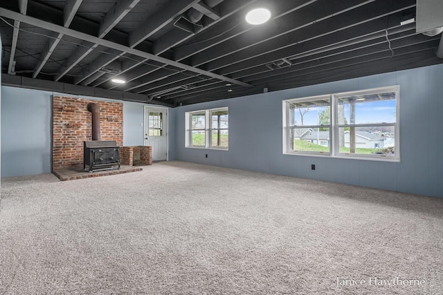 unfurnished living room with a wood stove, wooden walls, and carpet