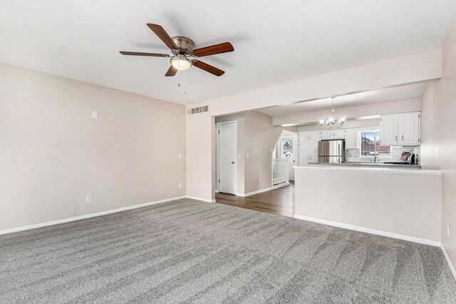 5984 Leisure S Dr SE, Grand Rapids, MI 49548 - unfurnished living room featuring a sink, dark carpet, ceiling fan with notable chandelier, baseboards, and visible vents