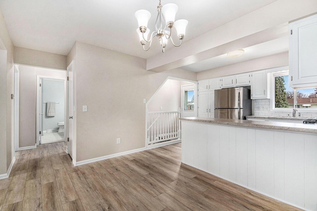 5984 Leisure S Dr SE, Grand Rapids, MI 49548 - kitchen with a notable chandelier, light wood finished floors, freestanding refrigerator, white cabinetry, and tasteful backsplash