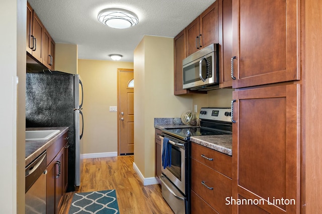 kitchen with light wood-style flooring, appliances with stainless steel finishes, dark countertops, baseboards, and a textured ceiling