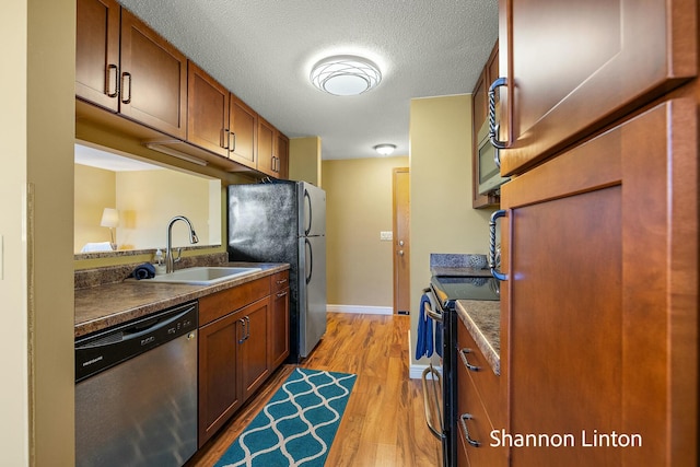 kitchen featuring light wood finished floors, a sink, brown cabinets, stainless steel appliances, and dark countertops