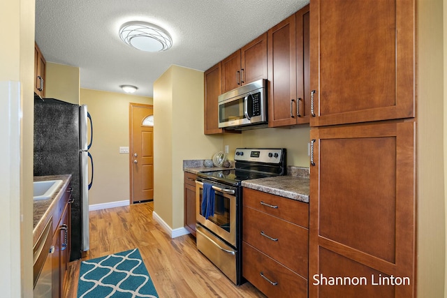 kitchen featuring light wood-style floors, baseboards, dark countertops, a textured ceiling, and appliances with stainless steel finishes