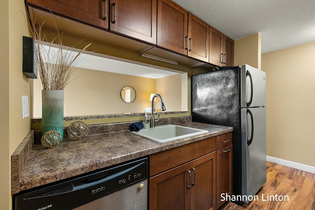 kitchen with light wood-style floors, appliances with stainless steel finishes, dark countertops, a sink, and a textured ceiling