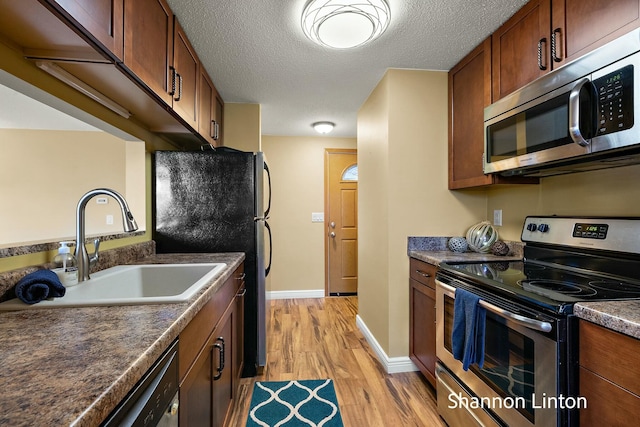 kitchen with appliances with stainless steel finishes, dark countertops, light wood finished floors, and a sink