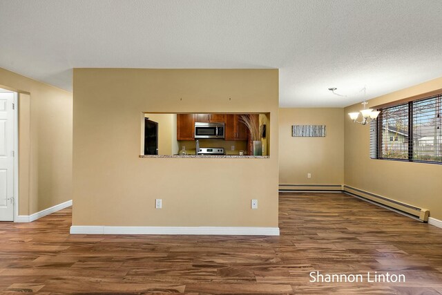 unfurnished living room with an inviting chandelier, dark wood-type flooring, a baseboard heating unit, and baseboards