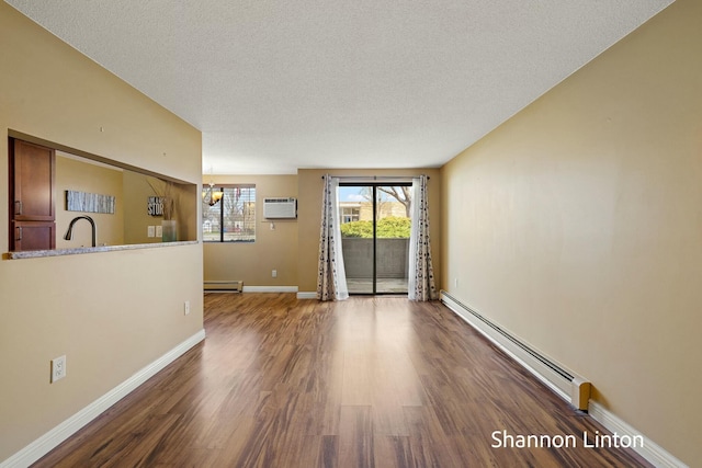empty room with a baseboard heating unit, a textured ceiling, and wood finished floors