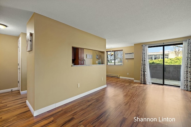 unfurnished living room featuring a wall unit AC, a chandelier, a textured ceiling, wood finished floors, and a baseboard radiator