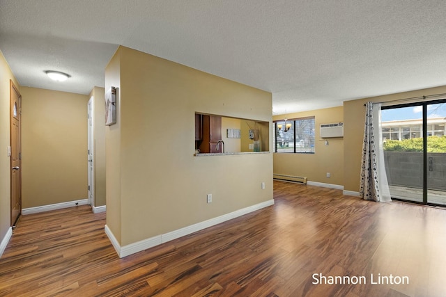 spare room with a wall unit AC, a notable chandelier, a textured ceiling, baseboard heating, and wood finished floors