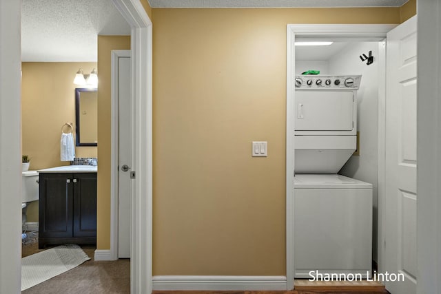 washroom featuring a sink, stacked washer and clothes dryer, baseboards, carpet floors, and laundry area