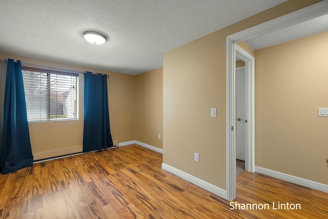 spare room featuring baseboards, wood finished floors, a textured ceiling, and a baseboard radiator