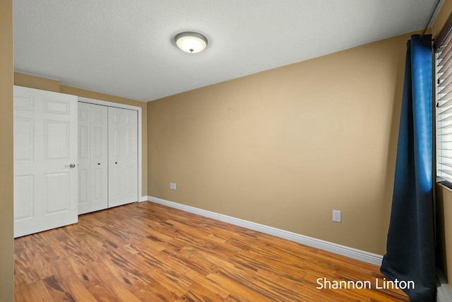 unfurnished bedroom featuring baseboards, wood finished floors, and a closet