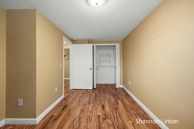 unfurnished bedroom with baseboards, wood finished floors, a textured ceiling, and a closet