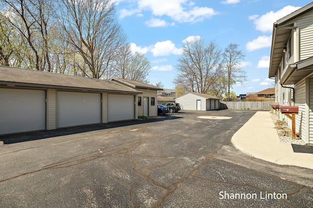 view of property exterior featuring fence, community garages, an outbuilding, and a residential view