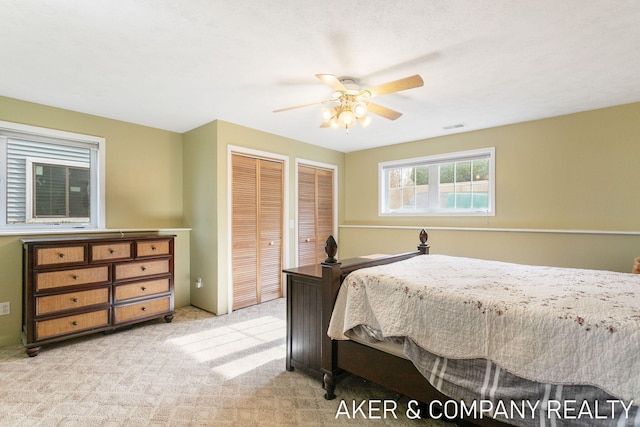 carpeted bedroom featuring a ceiling fan, multiple closets, and visible vents