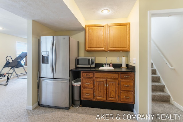 kitchen featuring a sink, appliances with stainless steel finishes, dark countertops, and light colored carpet