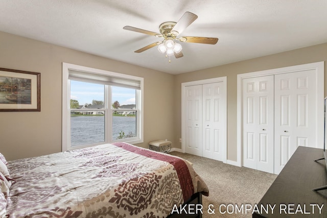 carpeted bedroom featuring baseboards, a ceiling fan, a water view, and two closets