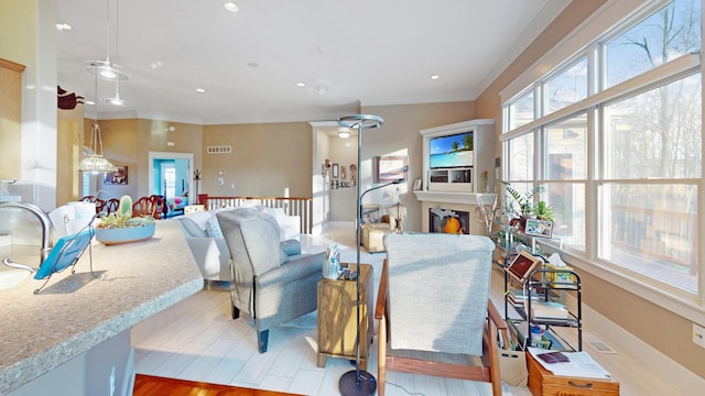 living area featuring visible vents, ornamental molding, a warm lit fireplace, and plenty of natural light