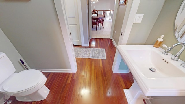 half bathroom featuring baseboards, toilet, wood-type flooring, and a sink