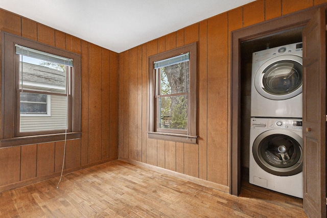 washroom featuring stacked washing machine and dryer, light wood finished floors, and baseboards