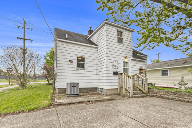 view of front of property with central air condition unit, a patio, a front lawn, and a chimney